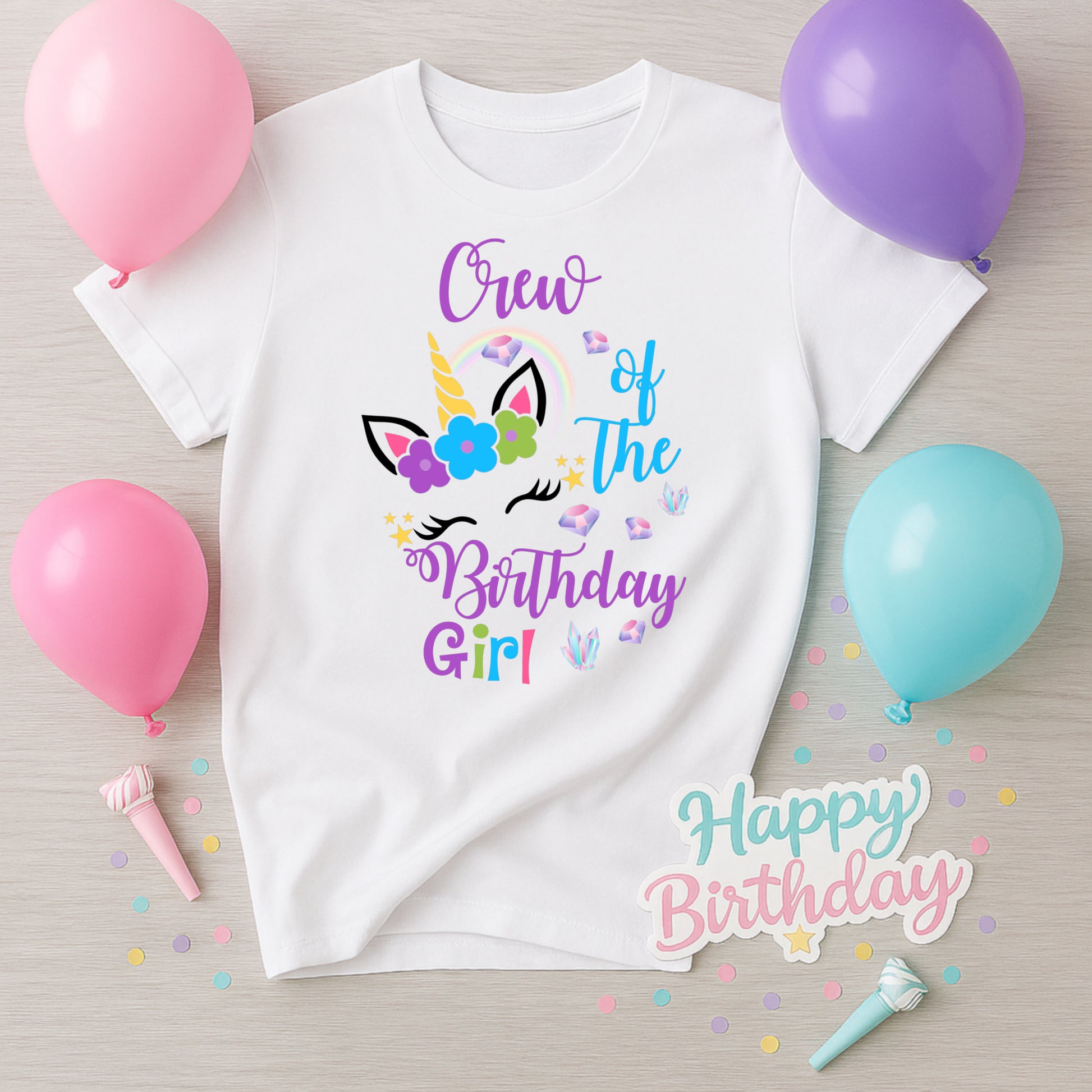 White t-shirt with 'Crew of the Birthday Girl' design surrounded by balloons and confetti on a wooden surface.