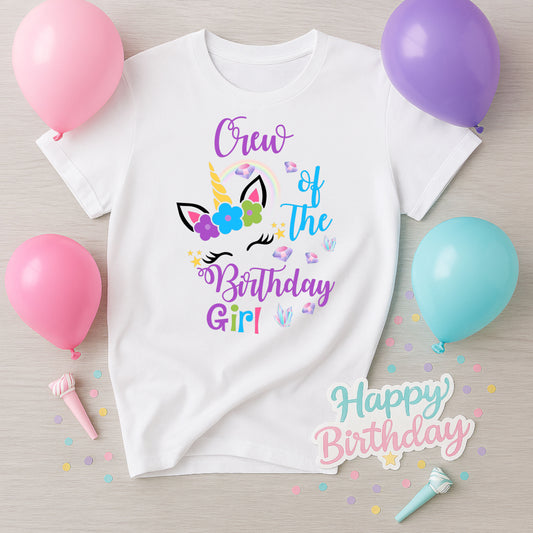 White t-shirt with 'Crew of the Birthday Girl' design surrounded by balloons and confetti on a wooden surface.