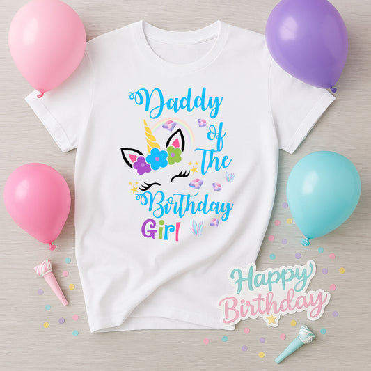 White t-shirt with 'Daddy of the Birthday Girl' text and unicorn design, surrounded by balloons and confetti on a wooden surface.